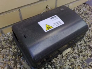 A black rodent poison box on the ground next to a brick wall