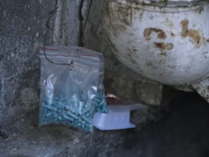 Two transparent plastic zip lock bags with blue rat poison pellets hanging on a wire